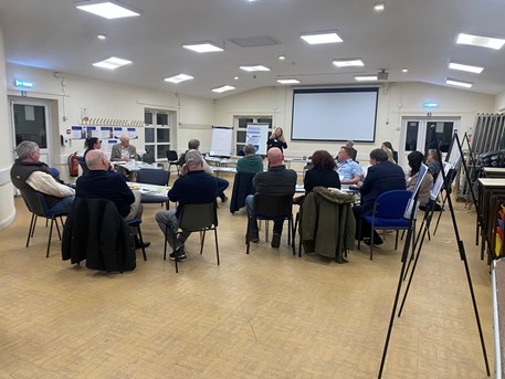 group of people sat in a hall listening to speaker standing in front of a flipchart