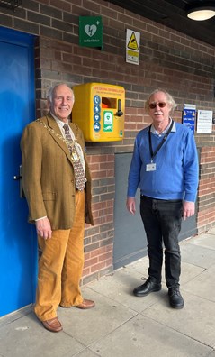 2 men smiling at camera standing in front of defibrilator